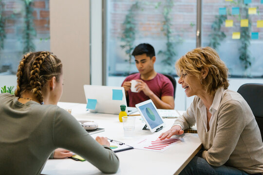 Female professionals discussing over business plan while businessman having coffee at desk