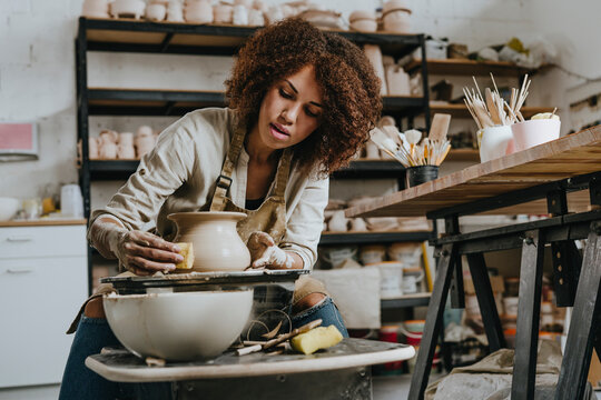 Young potter molding pot shape on pottery wheel at workshop