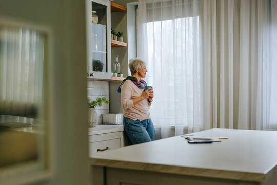 Woman relaxing in the kitchen looking out the window with a cup