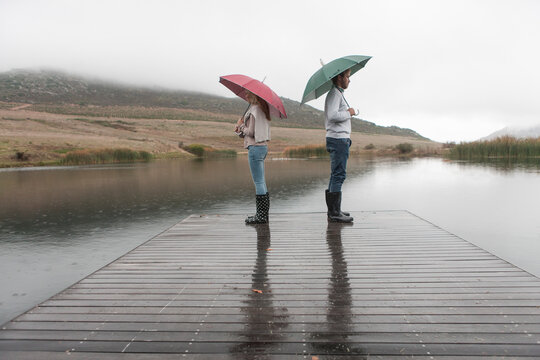 Couple standing in the rain on wooden boardwalk with umbrellas