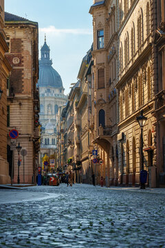 Beautiful view of Saint Stephen Basilica and historic architecture on a sunny cobblestone street in Budapest Hungary during golden hour with classic European city buildings