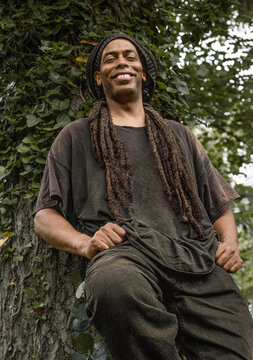 Happy man with dreadlocks relaxing against an ivy tree