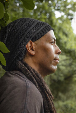 Thoughtful man with dreadlocks standing under a tree