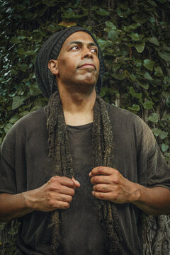Thoughtful man with dreadlocks standing against ivy wall
