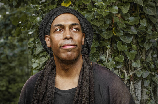 Man with dreadlocks and beanie looks up thoughtfully outdoors