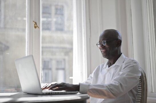 Happy senior Black man using laptop by a window