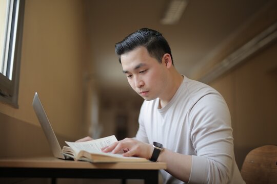 Focused Asian man reading a book at a desk