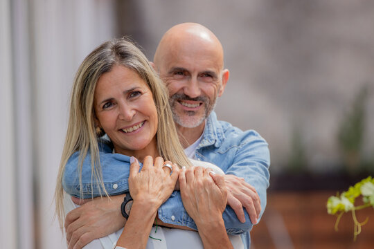Happy hispanic couple embracing outdoors, smiling woman with blonde hair and bald man in casual denim, sharing a tender moment