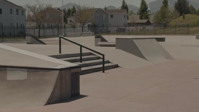 Slow left to right pan revealing concrete skatepark obstacles and open riding areas on a clear sunny day.
