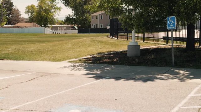 Smooth diagonal pan from shaded accessible parking sign area toward marked accessible parking spaces beside an open grassy park.