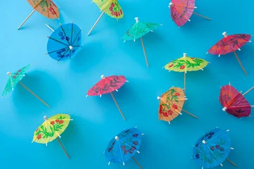 Colorful paper cocktail umbrellas scattered on a bright blue background, top view flat lay. Summer, tropical vacation and cocktail party celebration concept design with vibrant colors © Victor Moussa