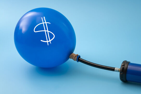 Blue balloon with a white dollar sign inflated by a hand pump on a blue background with copy space. Inflation, rising prices and money printing concept with text space for finance themes