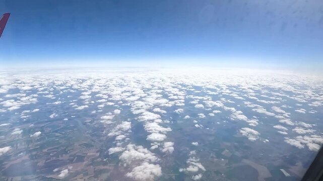 High-altitude aerial view of scattered white clouds over patchwork land and blue sky.