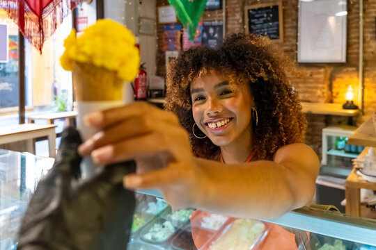 Happy woman receiving yellow ice cream cone in shop