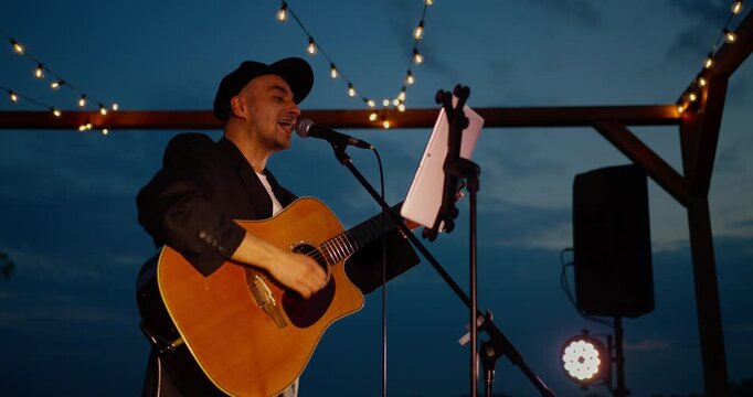 Male guitarist singing on an outdoor pergola stage at dusk