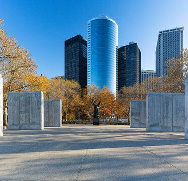 New York City travel destination showcasing the East Coast Memorial with eagle statue, framed by autumn trees and iconic Manhattan skyscrapers, representing urban exploration and tourism.