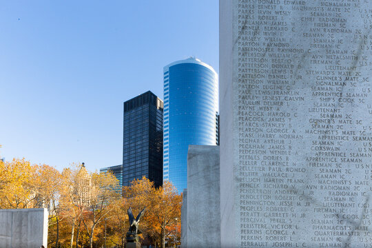 East Coast Memorial features names inscribed on stone pylons amidst autumn trees and urban skyscrapers, capturing historical tourism in Battery Park, New York City.