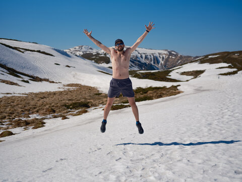 Happy shirtless man jumping on snowy slope in Carpathians