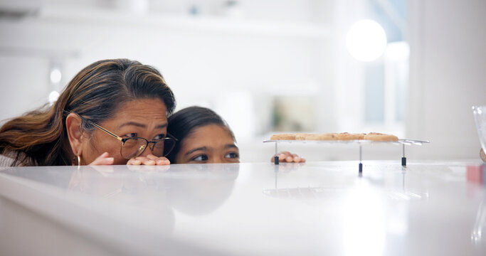 Grandmother, child and sneaky by kitchen counter for cookies, bonding or stealthy for sweet treats. Hungry, girl and senior woman in home with sugar craving, hide or sly with grandchild for biscuits.