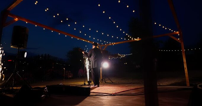 Male singer performing on wooden outdoor stage under string lights at night