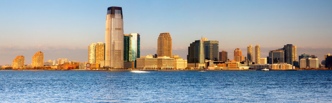 Jersey City skyline rises above the Hudson River waterfront at sunset, showcasing a prominent urban travel destination in Jersey City, New Jersey, USA.