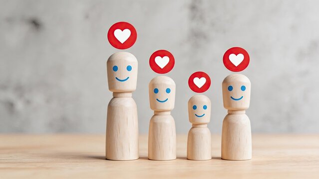 Wooden peg dolls representing a happy family with red heart icons above their heads, symbolizing love, affection, and social media likes on a wooden table.