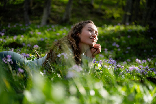 Harmony in nature. Side view portrait of a young woman lies on the grass in the forest, feeling freedom, love, and peace away from the bustle of the city. She admires the beauty of the park.