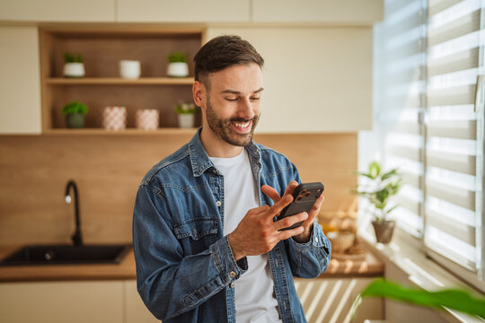 Young man smiling using smart phone in modern kitchen