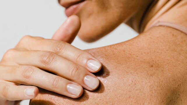 Close-up of a person applying moisturizer to their shoulder and upper back