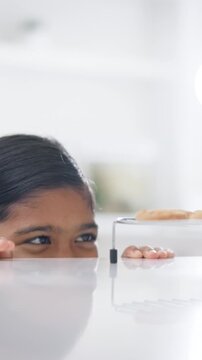 Peeking, child and steal in home with cookies, temptation and playful secret for dessert. Sneaky, girl and naughty with smile at house for baking craving, mischief and homemade treats for taste test