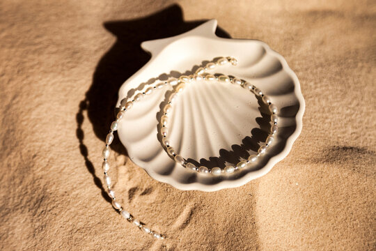 Pearl Necklace Resting on a Seashell Plate on Light Brown Beach Sand