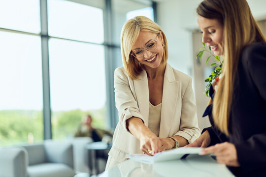 Businesswomen Collaborating at Modern Hotel Lobby Reception Discussing Reservation Documents and Plans