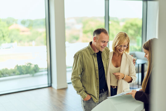Smiling Couple Reviewing Home Documents With Real Estate Agent During Modern Apartment Viewing