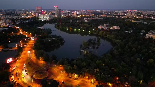 Nighttime aerial drone perspective of Bucharest cityscape, showing Herastrau park surroundings and the glowing modern office buildings in Pipera financial center, Romania.