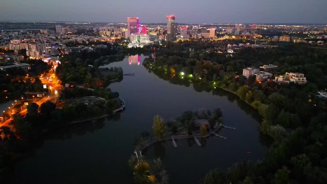 Nighttime aerial drone perspective of Bucharest cityscape, showing Herastrau park surroundings and the glowing modern office buildings in Pipera financial center, Romania.