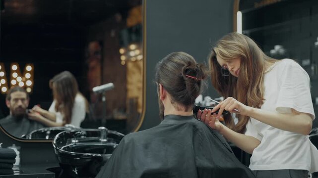 Barber trimming neck hair with electric clipper during beard grooming procedure in modern barbershop