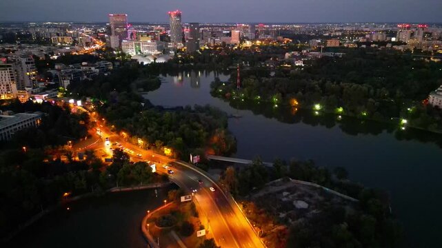 Nighttime aerial drone perspective of Bucharest cityscape, showing Herastrau park surroundings and the glowing modern office buildings in Pipera financial center, Romania.