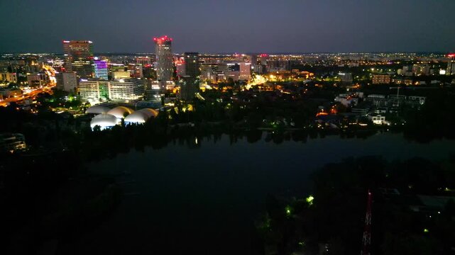 Nighttime aerial drone perspective of Bucharest cityscape, showing Herastrau park surroundings and the glowing modern office buildings in Pipera financial center, Romania.