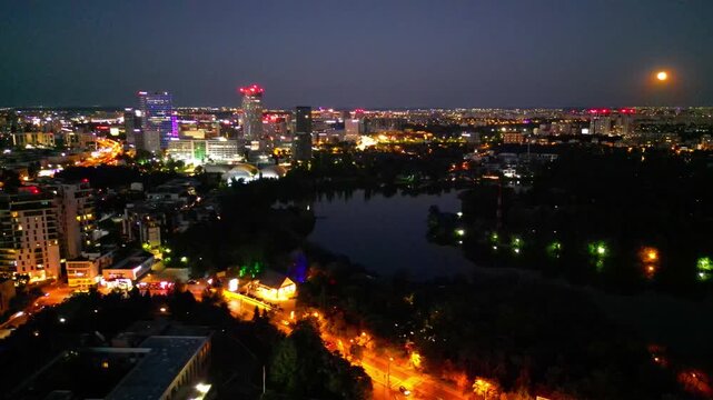 Nighttime aerial drone perspective of Bucharest cityscape, showing Herastrau park surroundings and the glowing modern office buildings in Pipera financial center, Romania.