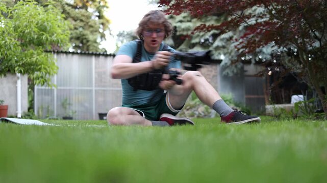 Young videographer practices advanced camera movement techniques while sitting on grass and controlling a gimbal stabilizer improving cinematic tracking skills and shot precision