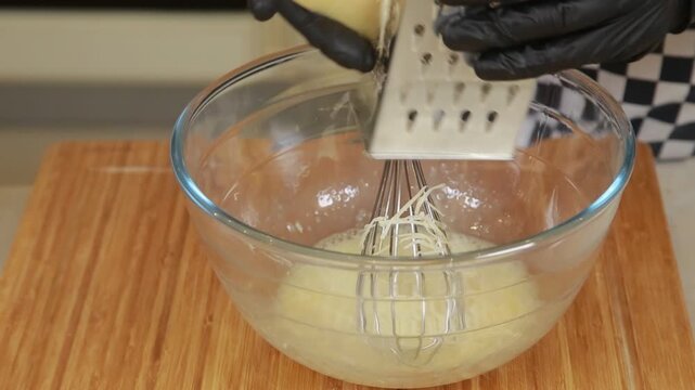 Chef is grating cheese in a glass bowl while cooking omelet