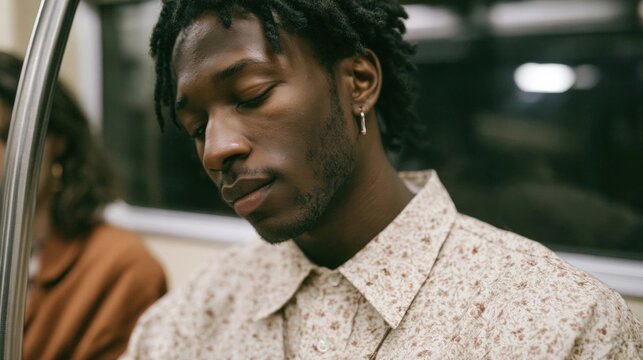 Young african-american man with dreadlocks, sitting on a subway train. he is wearing a white shirt with a floral pattern and has a serious expression on his face.
