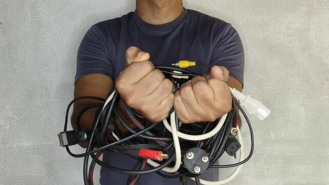 Technology addict person hand tied with tangled or messy different electrical power cord and cable wires of old electronic devices. Tech overload or addiction problem in young people awareness concept