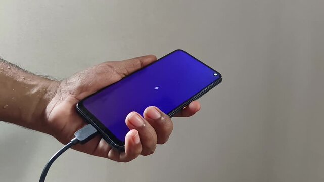Person hand holding smartphone and connect to power cable for using while recharging. Fast, turbo or quick charging mobile phone or device battery indicator animation on black display screen.