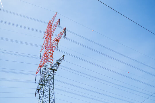 orizontal low-angle shot of an electricity transmission tower pylons with an orange painted top for aviation safety.