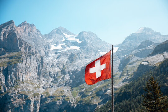 Swiss flag waving with scenic mountains in the background at Oeschinensee. Tourism in the Swiss Alps, Bernese Oberland, Switzerland