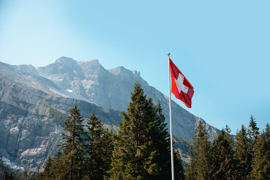 Swiss flag waving with scenic mountains in the background at Oeschinensee. Tourism in the Swiss Alps, Bernese Oberland, Switzerland