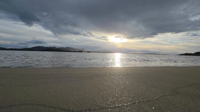 Premium 4K static shot of majestic sunset over Atlantic Ocean beach in Osaugen, Ulsteinvik, Norway. Calm sea waves roll onto sandy shore under dramatic evening sky. Scandinavian scenery.