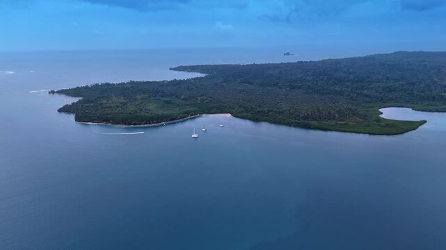 Overcast coastline with anchored yachts near Isla Bastimentos, Panama. Wide aerial shot of jungle covered peninsula, lagoon and moored boats on dark blue water.