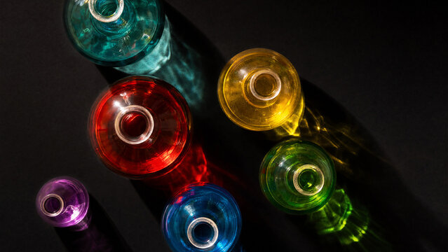 Colorful liquids in round glass demijohns creating light refraction, dark background, crisp details.